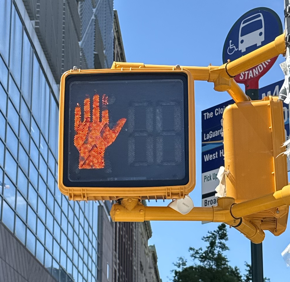 Orange hand on a city crosswalk signal with blue sky and signs