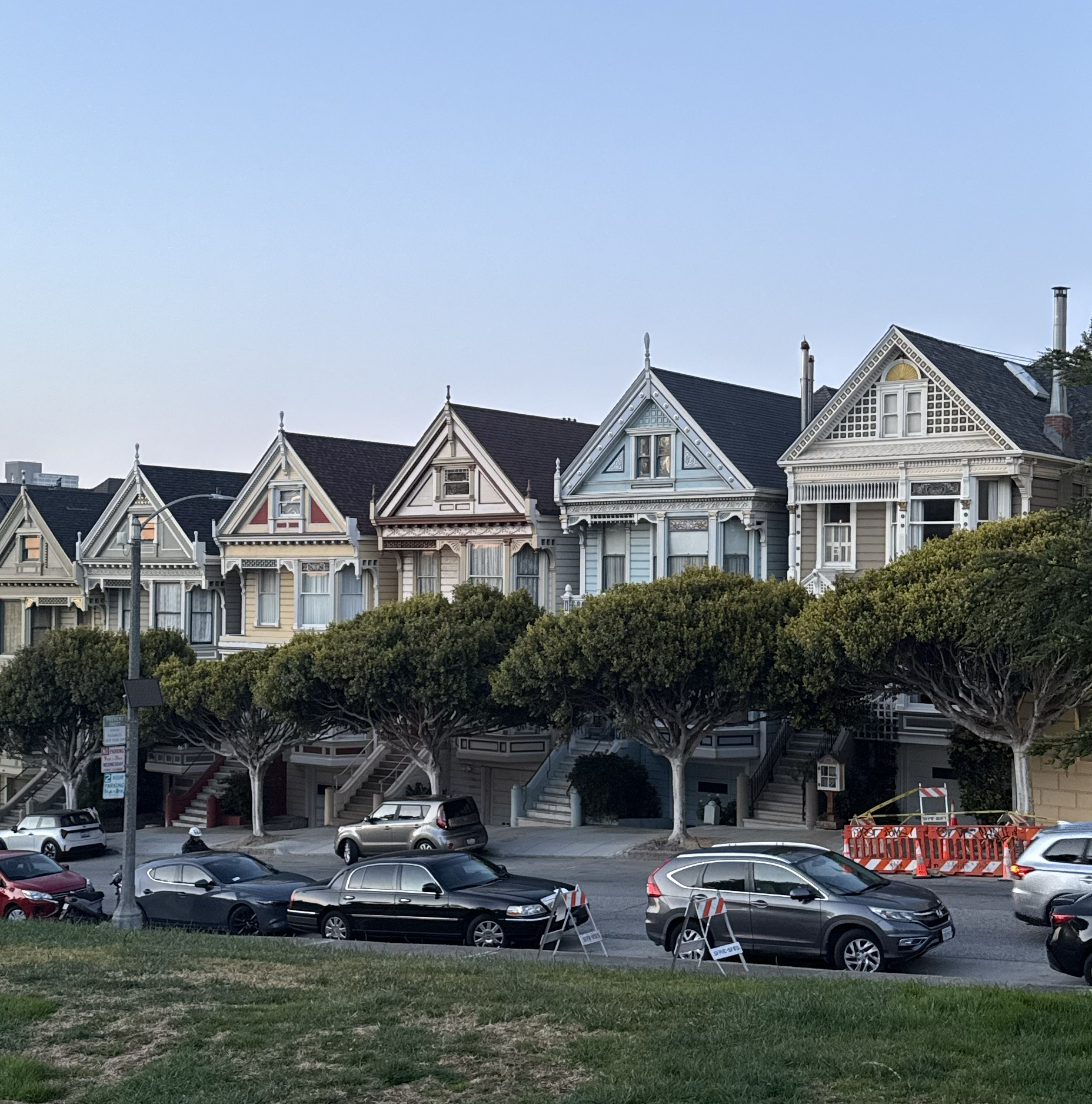 Row of colorful Victorian homes with trees and parked cars