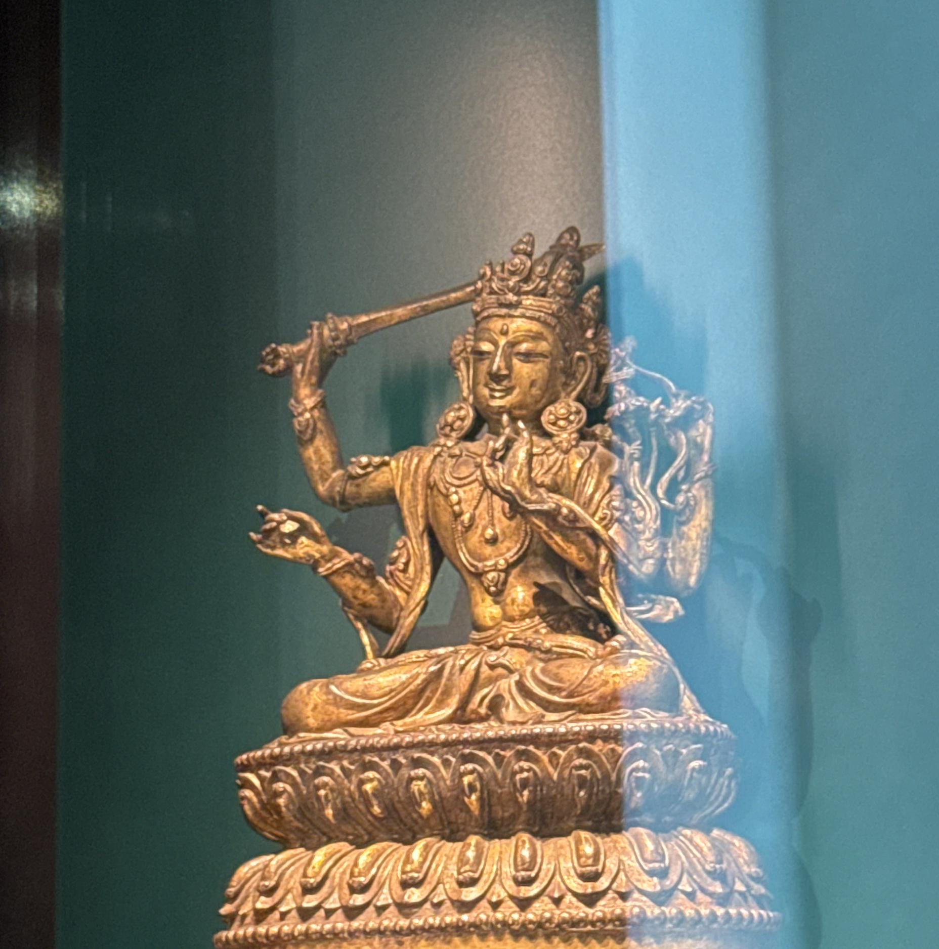 Gilded bronze Buddhist statue holding a sword, displayed in a case