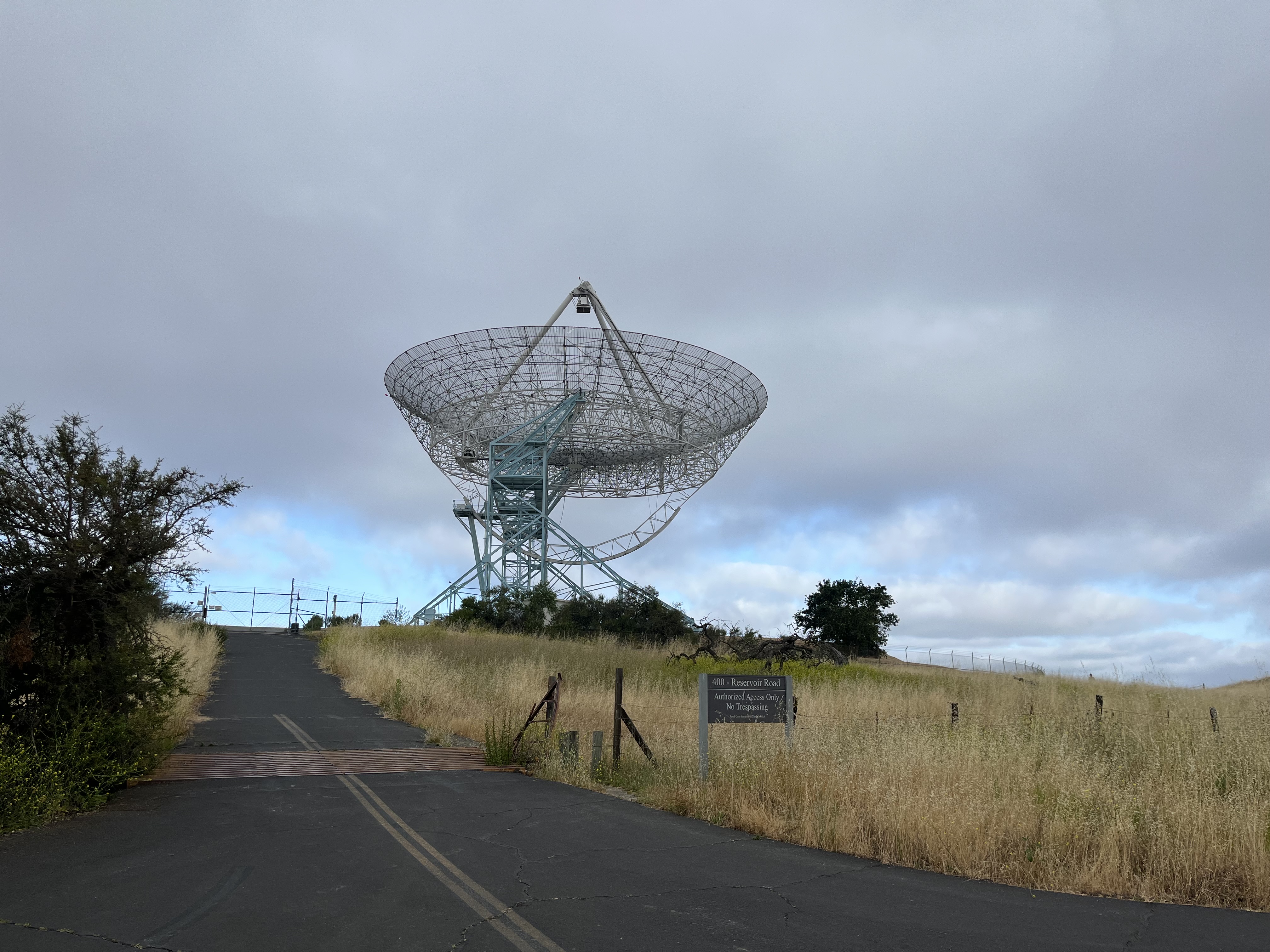 Large radio telescope dish on a hillside under cloudy sky